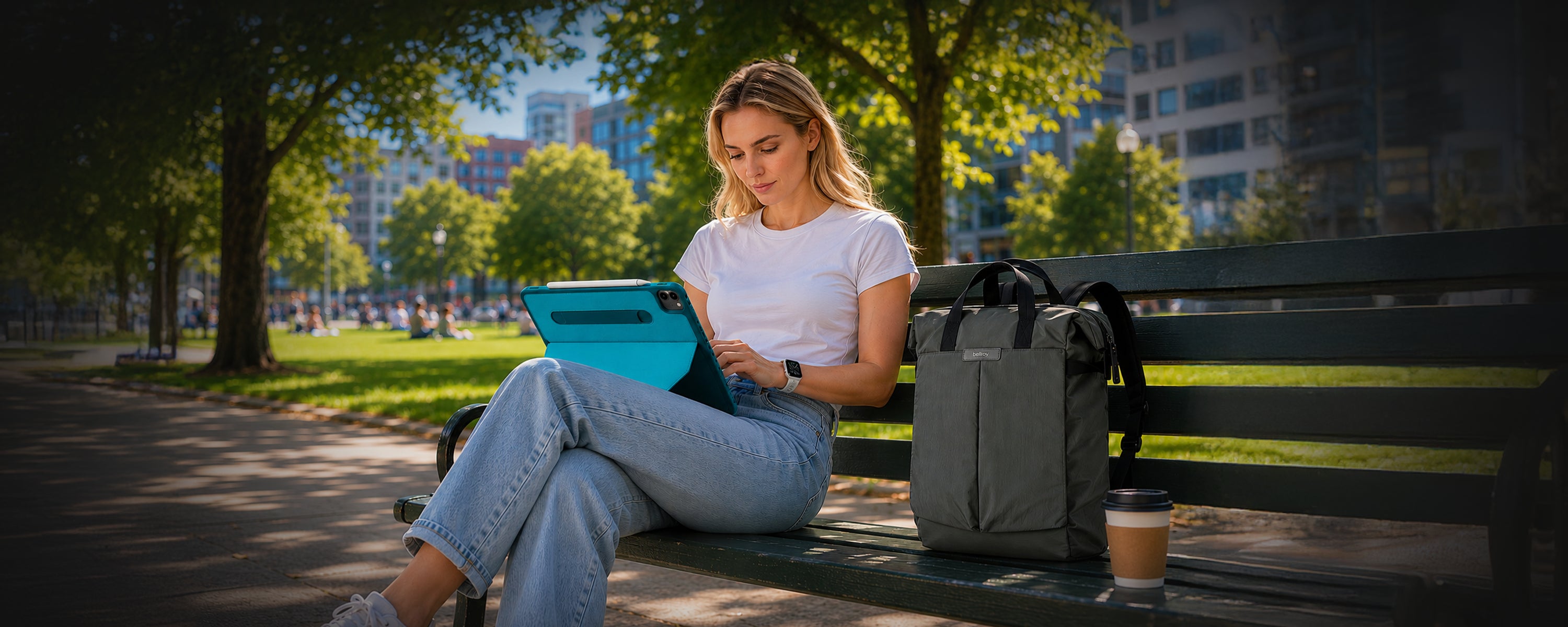 Woman using a laptop on a park bench with a cityscape in the background